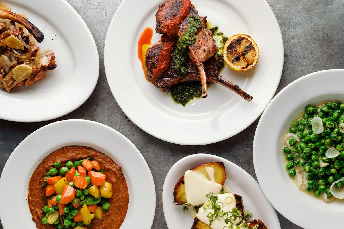 A variety of dishes on a table, including meat such as lamb chops, and vegetable dishes on the side