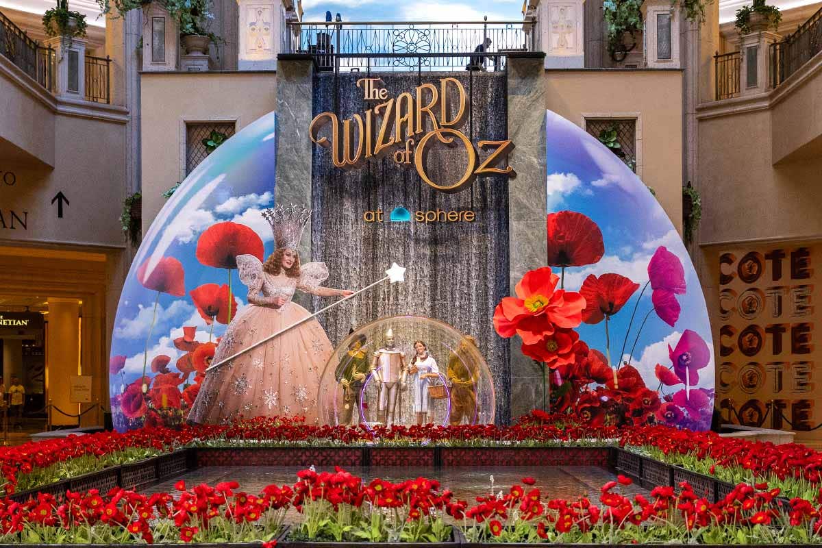 An interior waterfall surrounded by red poppies, with Glinda the Good Witch waving her wand over a plastic globe. Scarecrow, Tin Man, Dorothy and Cowardly Lion are visible through the globe.
