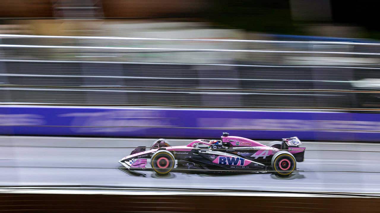 A BWT Alpine F1 car in focus against a blurred background of the track, blurred in a horizontal panned motion emphasizing the speed of the car