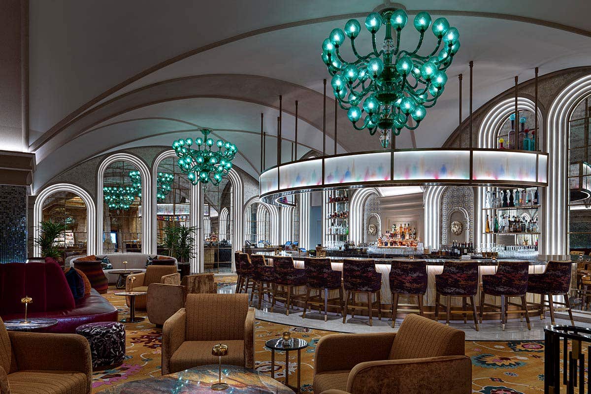 Elegant bar with arched ceiling, green chandeliers, and plush seating featuring a semi-circular bar counter.