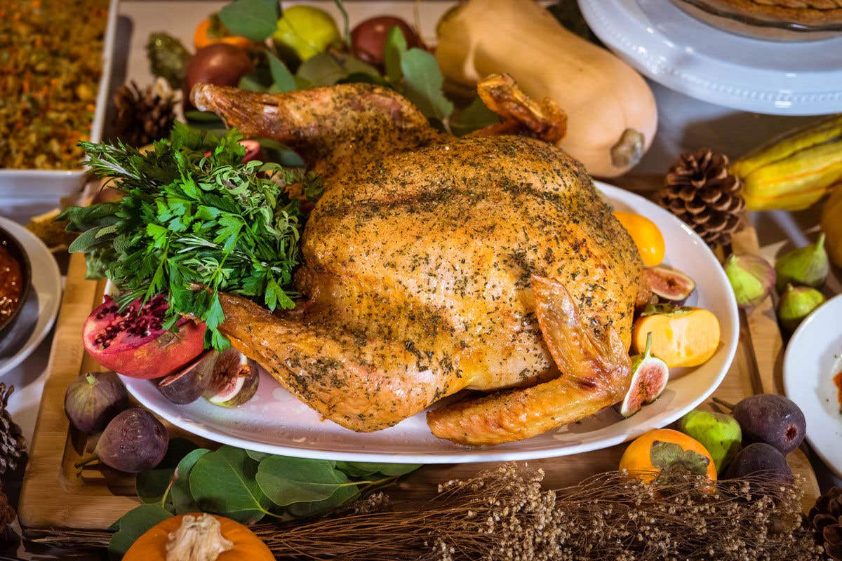 Cooked turkey on white platter surrounded by fall decor. 
