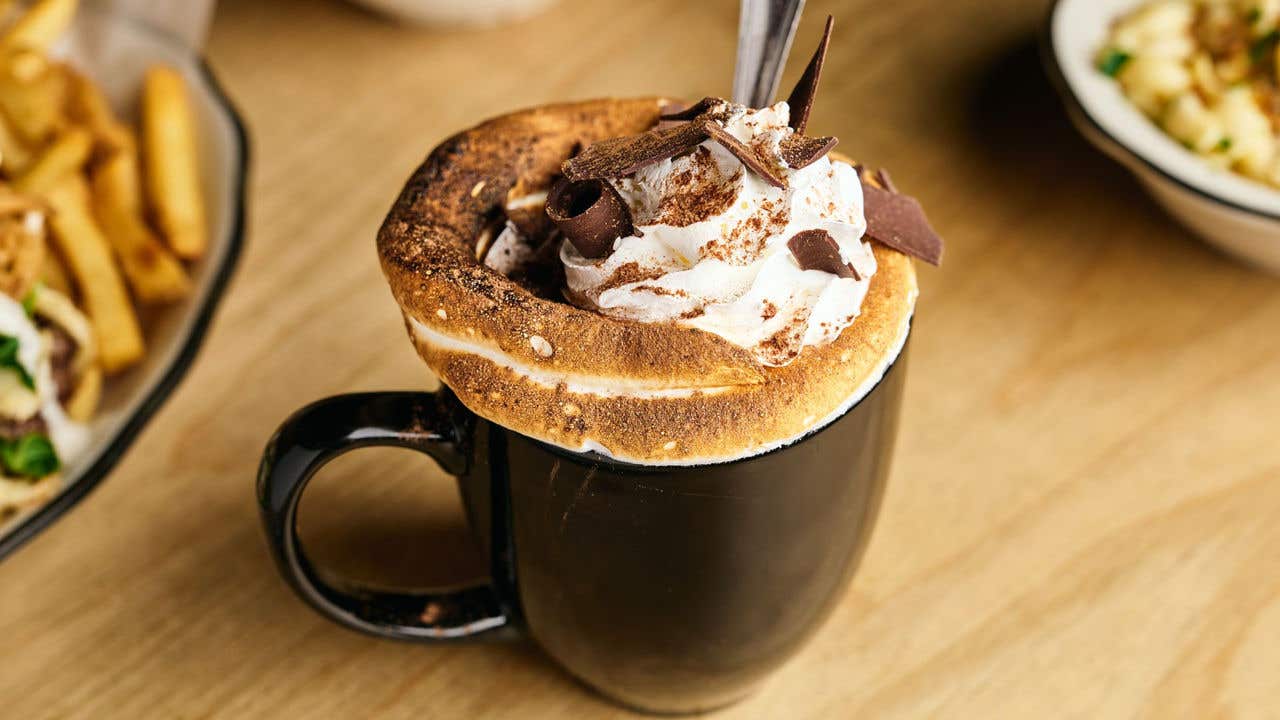 Cup of hot chocolate with whip cream, chocolate shavings and a straw on a table. 