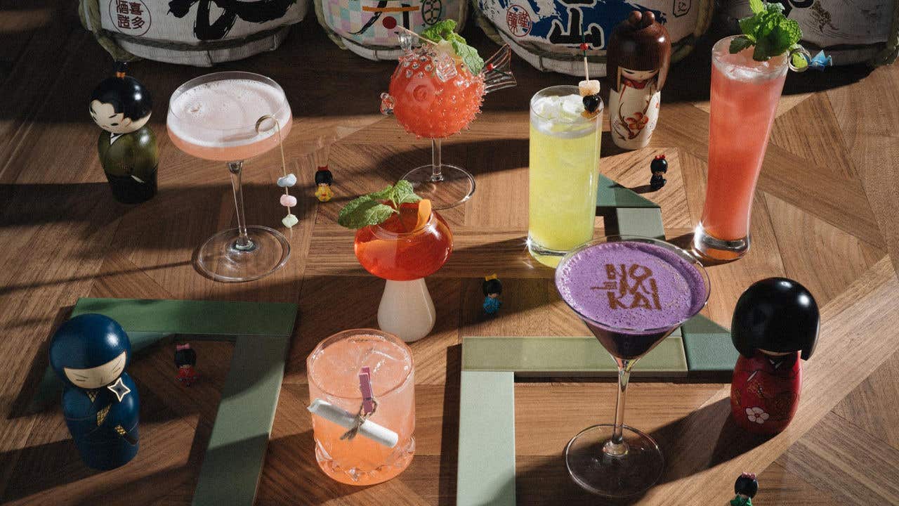 An arrangement of colorful cocktails with Japanese dolls on a wooden surface.