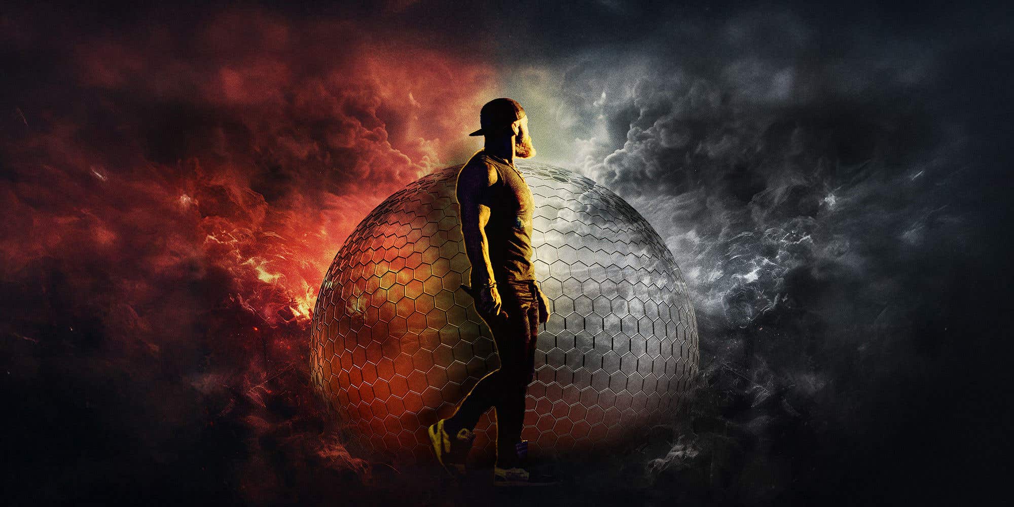 Zac Brown in casual attire holding a microphone in front of a large sphere made up of hexagons surrounded by gray smoke on the right and red smoke on the left.